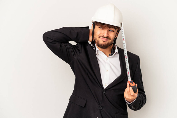 Young mixed race architect man wearing a helmet and holding meter isolated on grey background touching back of head, thinking and making a choice. - Photo, image