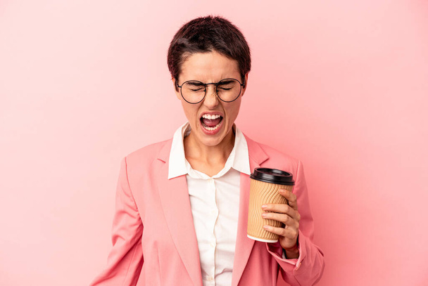 Young caucasian business woman holding a takeaway coffee isolated on pink background screaming very angry and aggressive. - Fotoğraf, Görsel