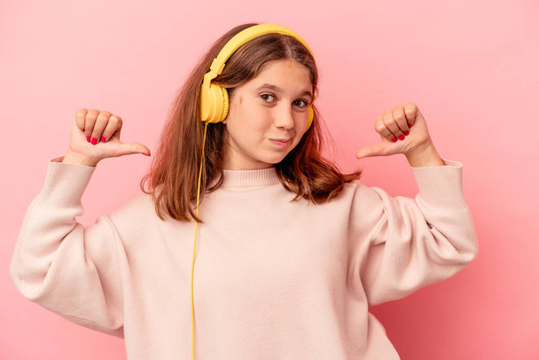 Petite fille caucasienne écoutant de la musique isolée sur fond rose se sent fière et confiante, exemple à suivre. - Photo, image