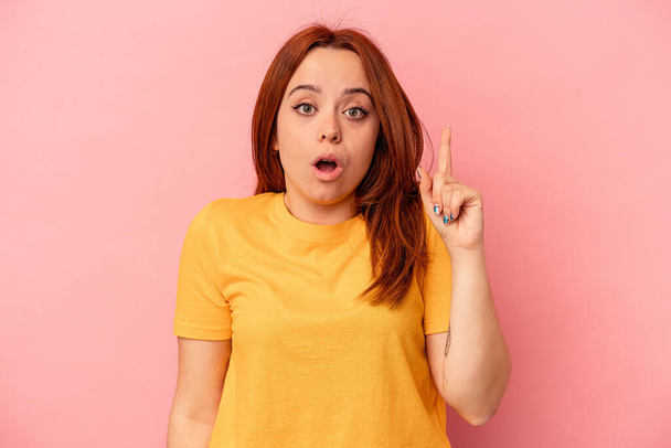 Young caucasian woman isolated on pink background pointing upside with opened mouth. - Photo, Image