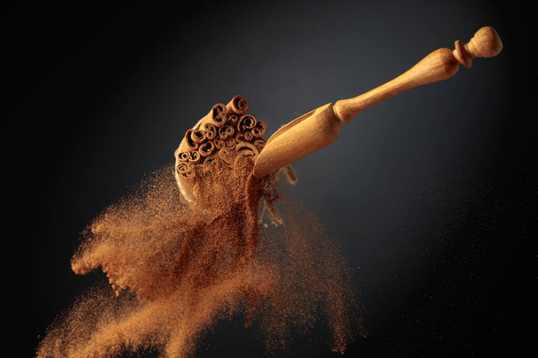 Cinnamon powder is poured out of the wooden spoon. The ground cinnamon and cinnamon sticks, tied with jute rope on a black background. - Φωτογραφία, εικόνα