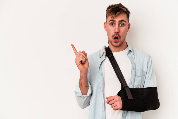 Young caucasian man with broken hand isolated on white background pointing to the side - Foto, imagen