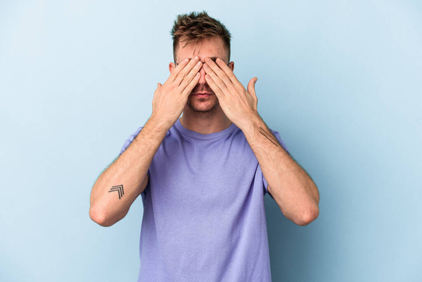 Young caucasian man isolated on blue background afraid covering eyes with hands. - Photo, Image