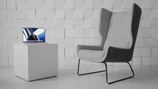 Laptop on a cubic shaped coffee table in a modern office. Action. Minimalistic design of the room with a comfortable chair and a computer on a small table. - Фото, зображення