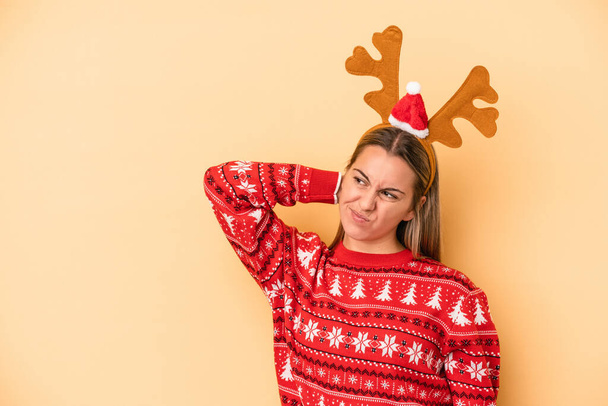 Young caucasian woman wearing a christmas reindeer hat isolated on yellow background touching back of head, thinking and making a choice. - Fotoğraf, Görsel