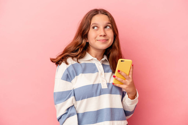 Klein blank meisje houden mobiele telefoon geïsoleerd op roze achtergrond dromen van het bereiken van doelen en doeleinden - Foto, afbeelding