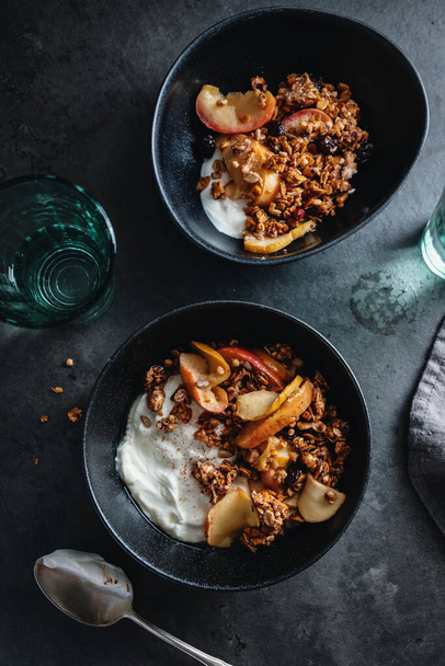 Appetizing homemade autumnal muesli with apples and yogurt served in bowl on dark background.  - Foto, Imagen
