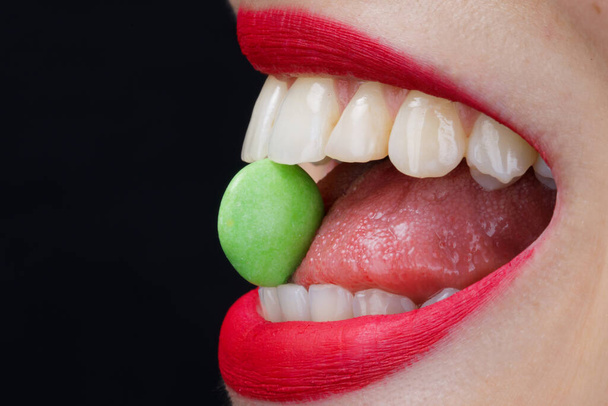 foto creativa de una sonrisa y dulces verdes en los dientes sobre un fondo negro - Foto, imagen