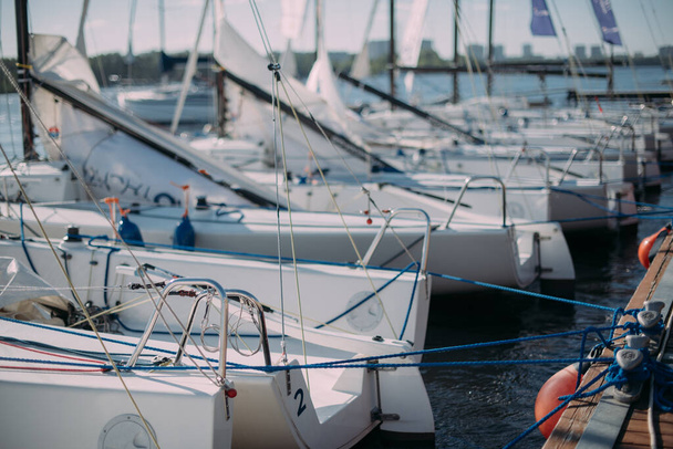 Sportjachtok vitorlázása kikötve a mólón egy napsütéses napon. Sok leeresztett vitorlás jacht áll a jachtiskola mólójának közelében. - Fotó, kép