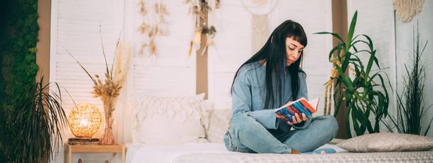 Jeune fille avec un journal intime sur le lit en pyjama bleu dans une chambre confortable. Belle femme brune écrit dans un journal intime de pensées, souvenirs dans des vêtements de maison confortables sur un grand lit - Photo, image