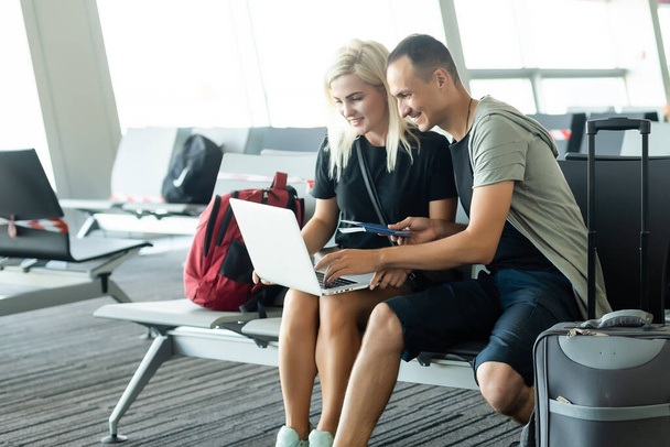 couple assis avec ordinateur portable, téléphone et valise dans la salle d'attente de l'aéroport. Concept de voyage d'affaires - Photo, image