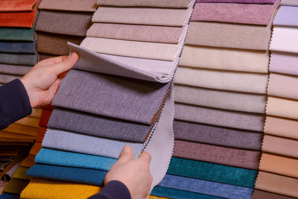 El cliente mira y selecciona la tela de color que le gusta, selecciona la tela de las muestras de tela para su nuevo sofá. - Foto, Imagen