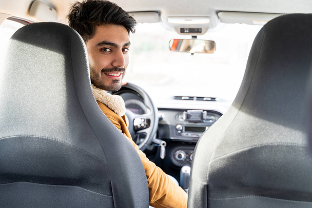 Man casually dressed with hand on driving wheel looking on backseat in camera - Photo, image