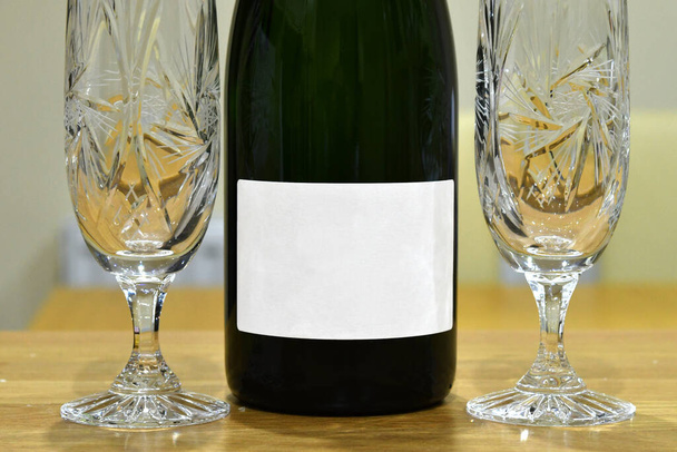 Dois copos de cristal vazios para champanhe com uma garrafa sem marca em uma mesa de madeira. Não há pessoas. - Foto, Imagem