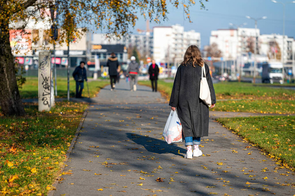 Riga, Latvia, October 29, 2021: woman with shopping bags on a sidewalk in a residential area of the city, rear view - 写真・画像