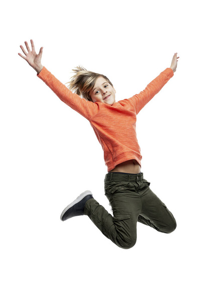 oyful boy is jumping. A child with a fashionable hairstyle in dark jeans and an orange sweater. Happiness, movement and positive. Isolated on white background. Full height. Vertical. - Zdjęcie, obraz
