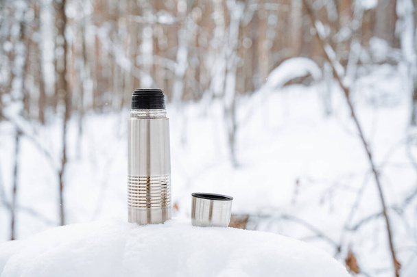 A cup of hot tea from a thermos. Drink coffee in nature. Metal thermal mug made of steel. A bottle that retains heat. Picnic utensils, camping kit. High quality photo - Fotografie, Obrázek