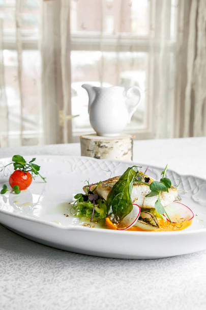 Plato de pescado - filete de lucioperca en plato sobre la mesa junto a la ventana, servido con tomate, salsa de rábanos y leche - Foto, imagen
