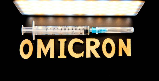 The word omicron made from wooden letters, syringe on a black background. Medical concept - Mutated coronavirus SARS-CoV-2 flu disease pandemic - Zdjęcie, obraz