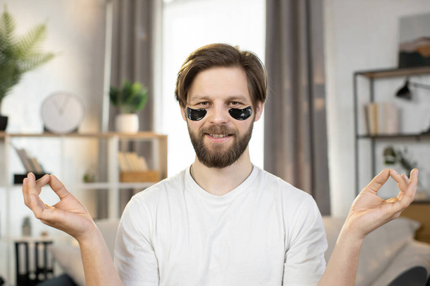 Caucasian man with anti-aging black eye-patches sitting with mudra hands at his workplace at home - Valokuva, kuva