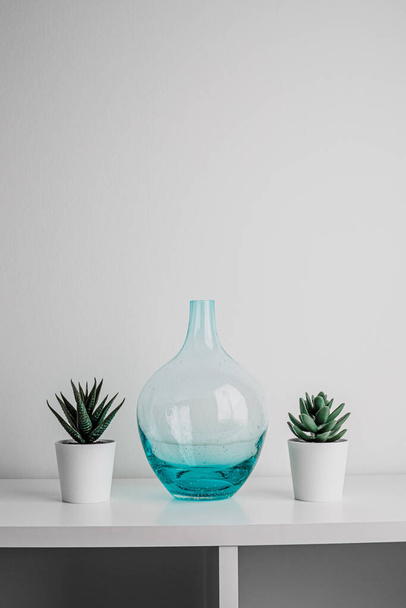 Decorative artificial ceramic and metal cactus, succulent and cactuses on white wall background. Light blue and mint glass vase. Home decoration. Side view. Copy space. - Foto, Imagen