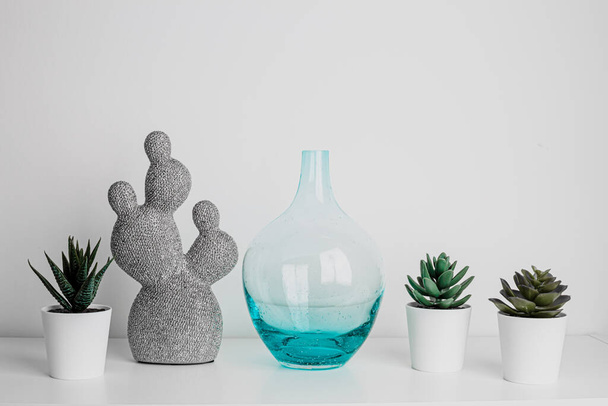 Decorative artificial ceramic and metal cactus, succulent and cactuses on white wall background. Light blue and mint glass vase. Home decoration. Side view. Copy space. - Fotografie, Obrázek