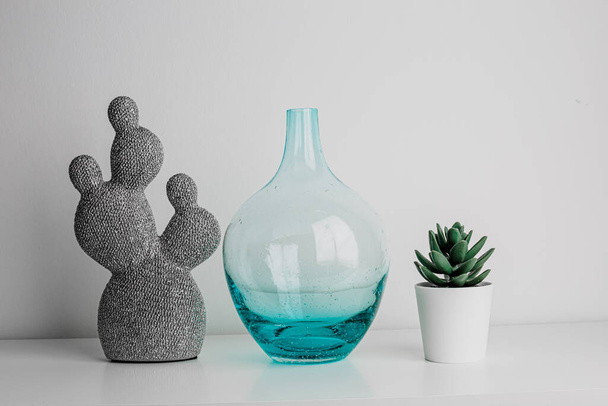 Decorative artificial ceramic and metal cactus, succulent and cactuses on white wall background. Light blue and mint glass vase. Home decoration. Side view. Copy space. - Foto, Imagem