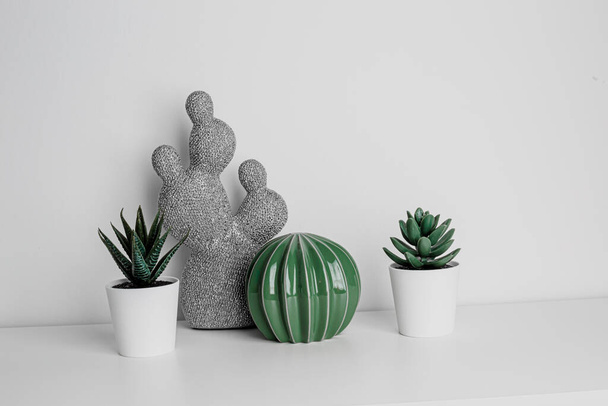 Decorative artificial ceramic and metal cactus, succulent and cactuses on white wall background. Light blue and mint glass vase. Home decoration. Side view. Copy space. - Photo, image