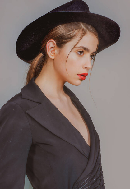 Young woman in fashion hat. Beautiful girl portrait. Fashionable and stylish woman in trendy hat, red lips makeup. Fashion look, beauty and style. Gray background. - Photo, image