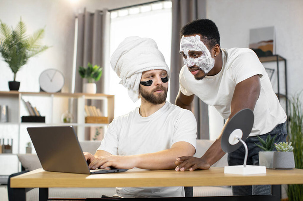 Young gay multiethnic couple, having cosmetic procedures, working on a laptop at home - Φωτογραφία, εικόνα
