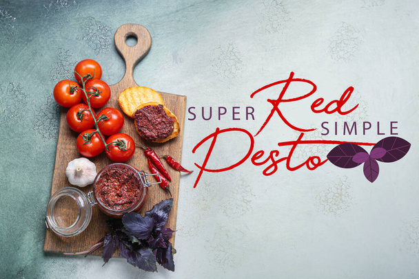 Houten bord met kruik van lekkere rode pesto saus en ingrediënten op grunge achtergrond - Foto, afbeelding