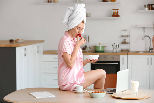 Pretty young woman eating strawberry in kitchen after shower - Photo, Image