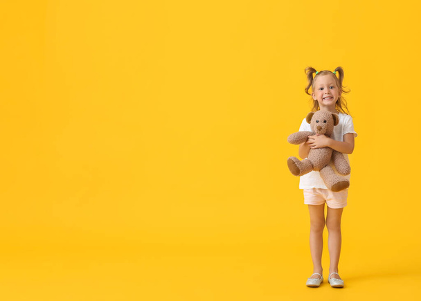 Adorable little girl with teddy bear on yellow background - Foto, Imagen