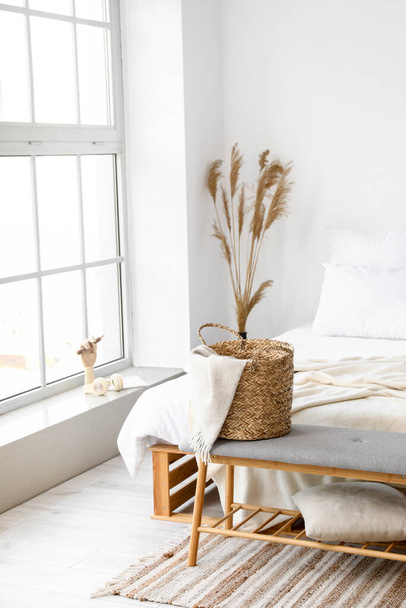 Banco suave con cesta de mimbre, cuadros y almohada en el dormitorio de luz - Foto, Imagen