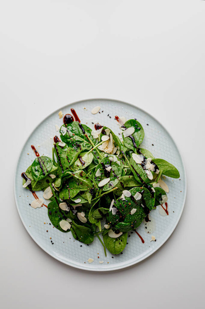 Spinach salad on white, with beetroot, arugula, balsamic vinegar, black sesame seeds, almond petals and feta cheese over light grey slate. Top view. - Zdjęcie, obraz