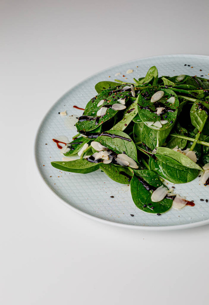 Spinach salad on white, with beetroot, arugula, balsamic vinegar, black sesame seeds, almond petals and feta cheese over light grey slate. Top view. - Foto, Imagen