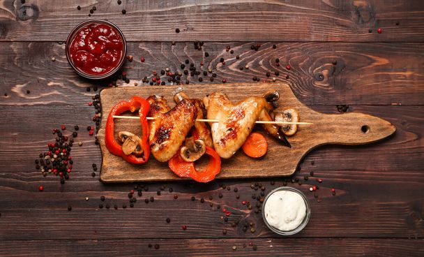 Bord met gegrilde kippenvleugels spiesjes en groenten op donkere houten ondergrond - Foto, afbeelding