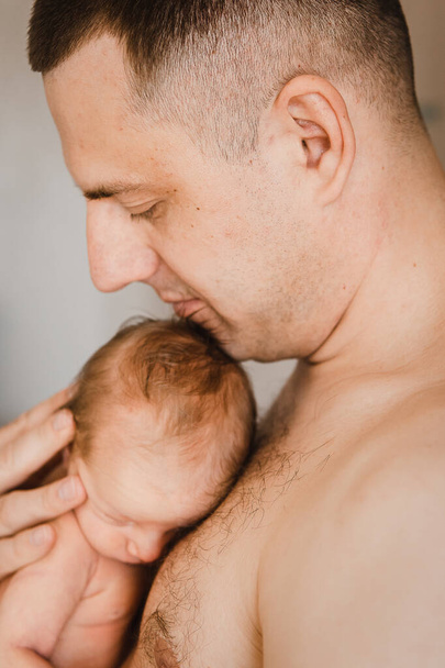 Close-up portrait of father holding sleeping newborn son on his arm. Head of newborn baby on fathers chest. Selective focus. Film grain - Fotografie, Obrázek