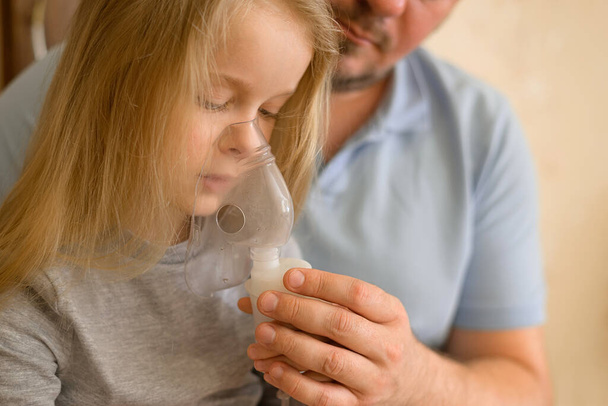 dad helps his sick child do inhalation with a nebulizer at home: he holds a mask from which steam. The father suspects that his daughter is ill. The child is not feeling well. the concept of equality - Foto, immagini