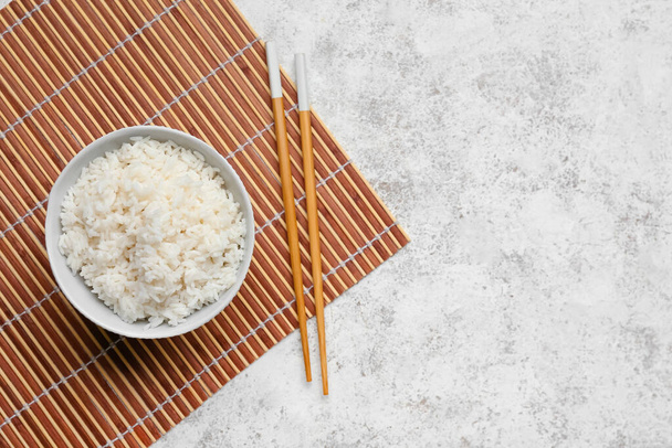 Miska ze smacznym gotowanym ryżem i pałeczkami na jasnym tle - Zdjęcie, obraz