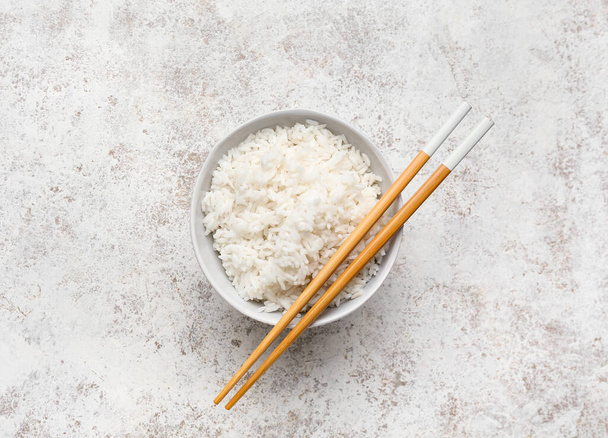Чаша с вкусным варёным рисом и палочками для еды на светлом фоне - Фото, изображение