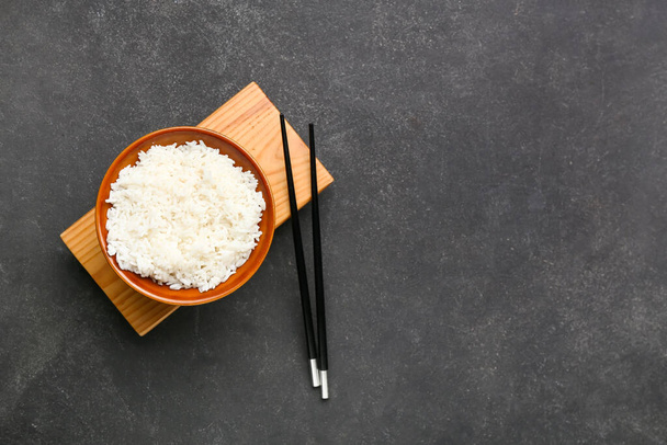 Bowl with tasty boiled rice and chopsticks on dark background - Φωτογραφία, εικόνα
