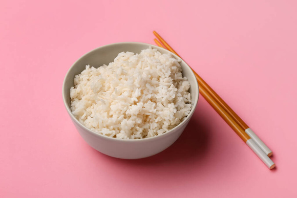 Cuenco con sabroso arroz hervido y palillos sobre fondo rosa, primer plano - Foto, imagen