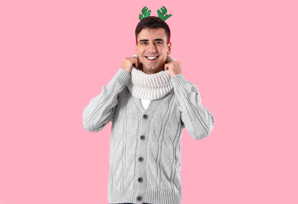 Красивый молодой человек в теплом свитере и с оленьими рогами на цветном фоне - Фото, изображение