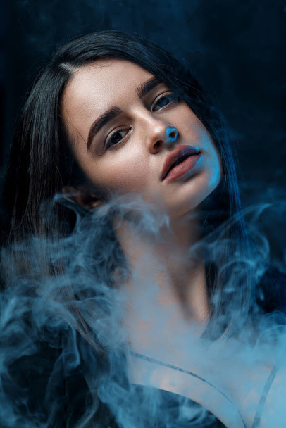 retrato close-up de uma bela jovem morena com maquiagem profissional em uma jaqueta preta no estúdio. luz multicolorida com fumaça. - Foto, Imagem