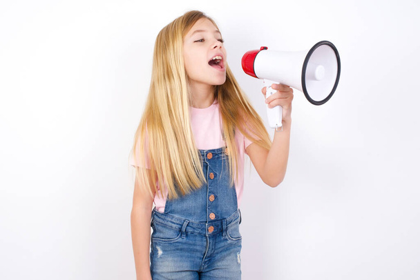 beautiful caucasian little girl wearing denim jeans overall over white background Through Megaphone with Available Copy Space - Fotó, kép