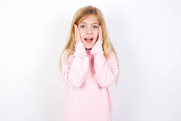 hermosa niña caucásica vistiendo suéter rosa sobre fondo blanco agradable mirada alegre, feliz reacción - Foto, imagen