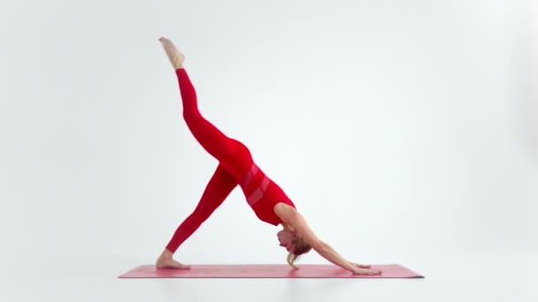 Millennial woman stretching in yoga pose meditation isolated on white background in red Sportswear. Portrait of young female yoga practitioner posing for copy space. 4k - Séquence, vidéo