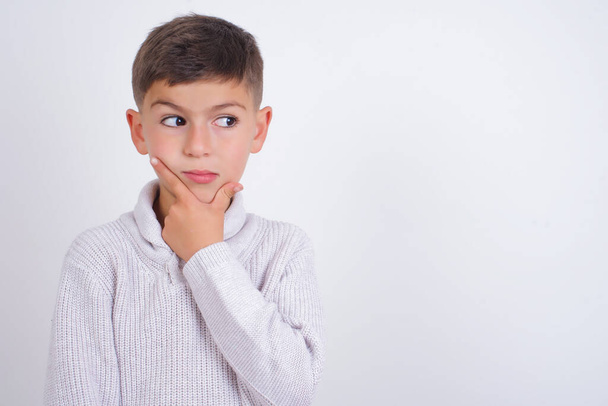 Caucasian kid boy wearing knitted sweater standing over white background Thinking worried about a question, concerned and nervous with hand on chin. - Photo, Image