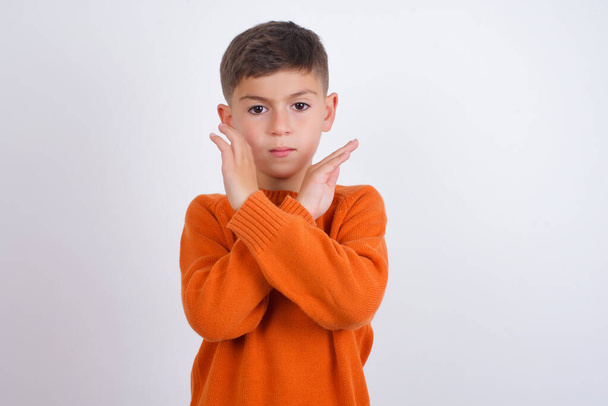 Biały chłopiec ubrany w pomarańczowy sweter stojący nad białym tłem Odrzucenie wyrażenie skrzyżowanie ramion robiące negatywny znak, wściekła twarz - Zdjęcie, obraz